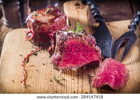 Rare Boar Filets Seasoned with Fresh Herbs on Wooden Cutting Board with Metal Serving Utensils