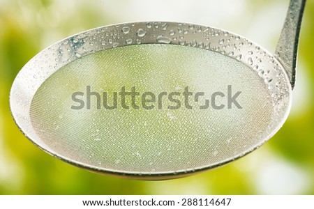Close Up of Clean Metal Strainer Covered with Rain Water Drops Outdoors with Fresh Green Vegetation Background