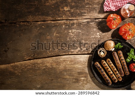 Grilled barbecued sausage with portobello mushrooms and fresh tomato on an old rustic wooden with cracks viewed from above, copyspace