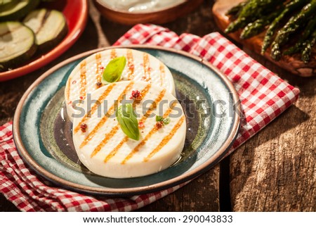Rounds of Grilled Firm Cheese with Grill Marks Garnished and Resting on Plate on Red Checkered Napkin on Rustic Wooden Table at Barbeque Party