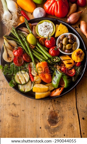 High Angle View of Bounty of Colorful Grilled Vegetables and Olives on Cast Iron Pan Resting on Wooden Table Surface with Copy Space in Foreground