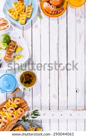 High Angle View of Grilled Fruit and Seafood Dishes Scattered on White Wooden Table Surface with Copy Space