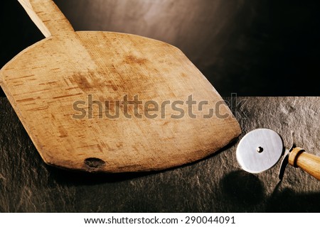 Wooden Pizza Paddle Board and Circular Pizza Cutter, Tools of the Trade on Dark Textured Counter Surface
