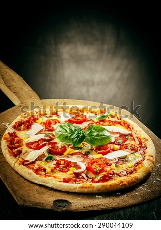 Close Up of Fresh Baked Pizza Topped with Tomatoes, Basil and Cheeses Served on Wooden Pizza Paddle with Dark Grey Background with Copy Space