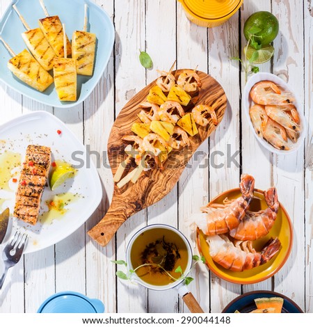 High Angle View of Grilled Fruit and Seafood Dishes Arranged on White Wooden Table Surface