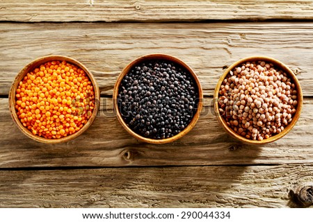Bowls of assorted dried lentils with red lentils, black beluga lentils and mountain lentils displayed on an old textured wooden table viewed from above