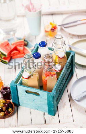 Fresh fruit juice and milk in glass bottles in a colorful rustic wooden crate on a picnic blanket outdoors in summer sun with watermelon for dessert