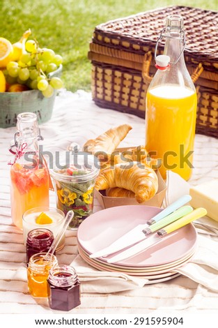 Fruit juice, croissants and fresh fruit for a summer picnic laid out on a blanket on a green lawn with a rustic wicker hamper