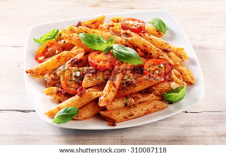 Close up Gourmet Tasty Spicy Italian Penne Pasta with Tomato and Herbs on a White Plate, Served on Top of a Wooden Table.