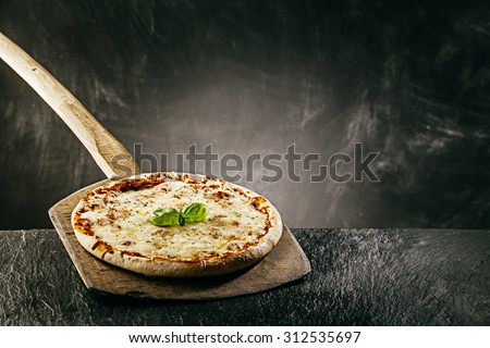 Steaming hot tasty margarita Italian pizza fresh from the pizza oven in a pizzeria served on a long handled wooden board with copyspace behind