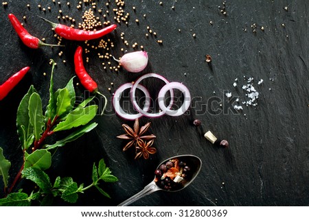 High Angle View of Various Fresh Herbs and Spices, Onion Slices, and Hot Peppers Scattered on Dark Gray Stone Surface with Copy Space