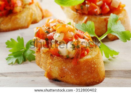 Close Up of Fresh Tomato Bruschetta Appetizers on Crisp Crusty French Baguette Bread Slices Garnished with Fresh Herbs on White Wooden Table Surface