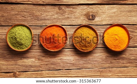 Row of colorful spices in bowls viewed from above on a wooden table with ginger, cayenne chili powder, turmeric and matcha or amchoor for Asian cuisine