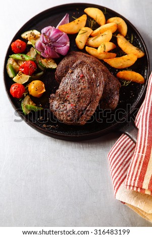 High Angle View of Tasty Roasted Beef Steak with Grilled Veggies on Iron Cast Skillet, Served on the Table for Dinner.