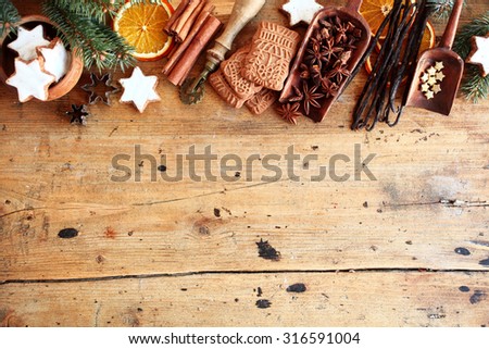 Traditional Christmas spices and cookies arranged as a top border over rustic wood background with cinnamon, star anise, speculoos and star biscuits and dried orange slices, large copyspace