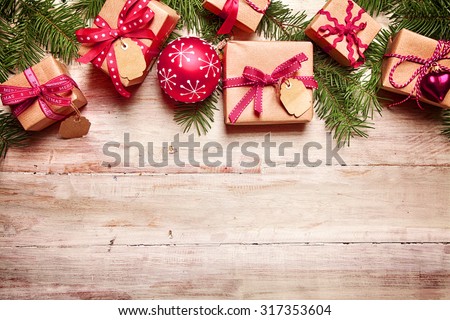 Festive Christmas border with gifts tied with red ribbon, matching red baubles and fresh pine foliage over rustic wood with copyspace for your seasonal greeting