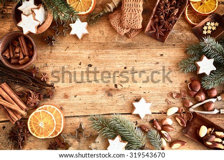 Traditional Xmas frame with spices, speculoos biscuits, star cookies and assorted nuts decorated with dried orange around central copyspace on a rustic wood background for your Christmas message