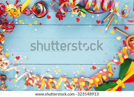 Festive party border or frame of colorful spiral streamers and confetti arranged on a rustic old blue wooden background with a bow tie in the corner and copyspace