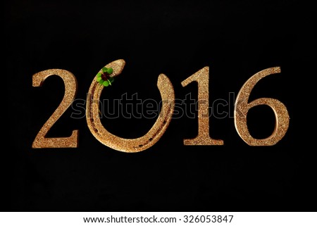 2016 New Year background wishing you Good Luck with a golden horseshoe incorporated into the date with a green four-leaf clover or shamrock on a black background