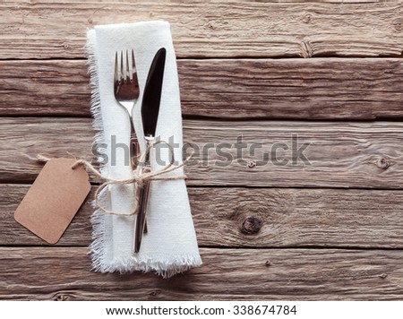 High Angle View of Silver Knife and Fork Tied with String and Blank Tag on White Napkin with Fringed Edges on Rustic Wooden Table with Copy Space