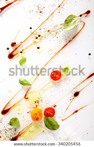 Colorful cooking ingredients abstract background with swirled soy sauce, pepper, halved cherry tomatoes and fresh green basil leaves on a white background