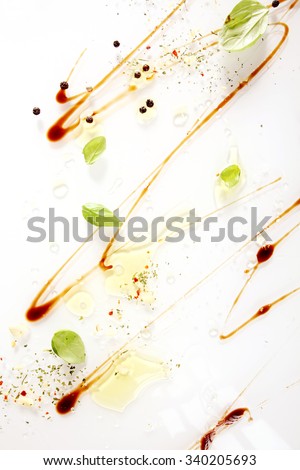 Abstract Italian and Mediterranean healthy cooking background with an artistic zigzag swirl of soy sauce with olive oil, ground spices and fresh green basil leaves on white