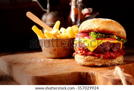 Hot chilli pepper cheeseburger with spicy chili sauce, a beef patty and melted cheese served with a side dish of crispy French Fries on a wooden board in rustic restaurant
