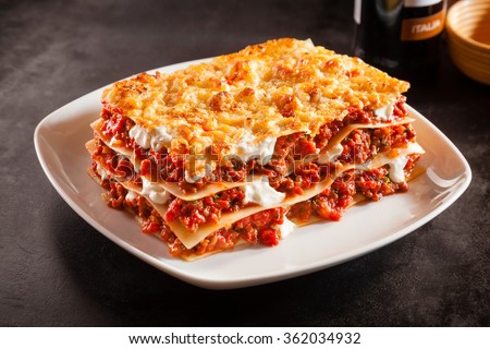 Tomato and ground beef lasagne with cheese layered between sheets of traditional Italian pasta served on a white plate on a dark restaurant or bar counter