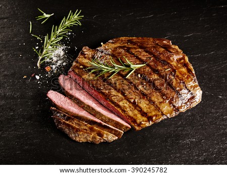 Single roasted medium rare sliced flank beef piece with rosemary over dark table background