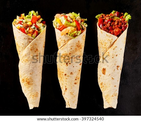 High Angle Still Life of Trio of Tex Mex Fajita Wraps on Black Background - Variety of Grilled Flour Tortilla Wraps Stuffed with Different Fillings Such as Chicken and Chili
