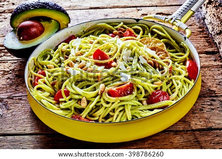 Tasty Italian fettuccine pasta cooked with avocado pear, fresh tomato and pine nuts garnished with grated parmesan and serving in a rustic frying pan on an old wooden table