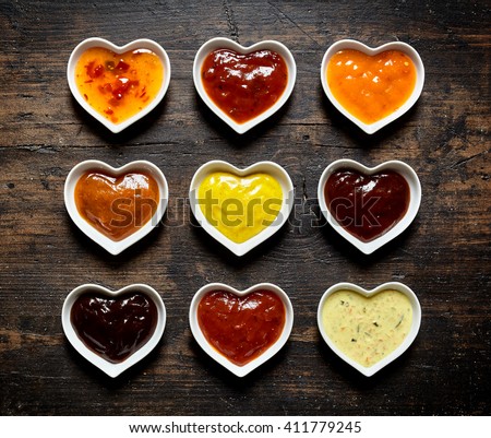 Top down view on nine colorful mild and spicy sauces and marinades filled up inside heart shaped bowls over weathered wooden table