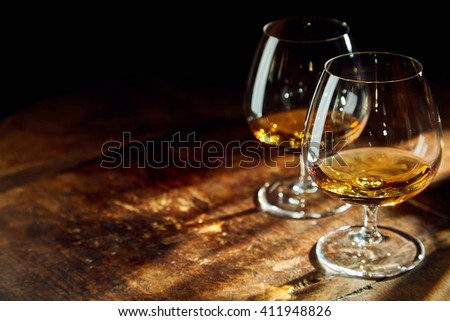 Close up of two bourbon filled glasses on wooden table in a dark room with a few rays of sunlight