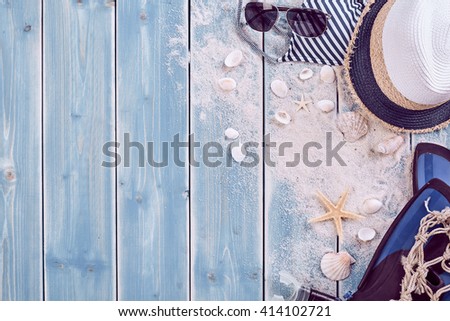 Summer vacation relaxation background theme with seashells, loose sand, hat, sunglasses and weathered wood blue background with copy space