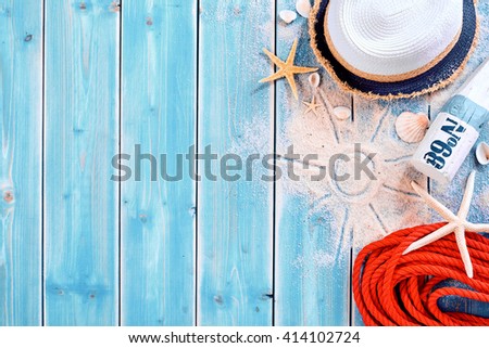 Summer vacation beach background theme with seashells, shape of sun in sand, red rope, sun tan bottle and hat with copy space over painted blue wood planks