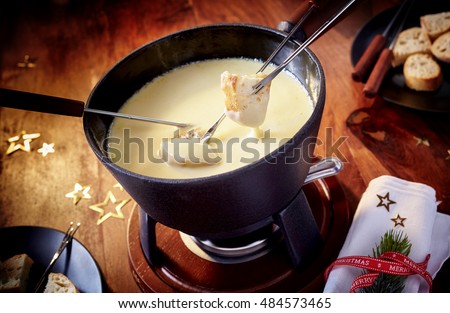 Dipping bread into a delicious cheese fondue during the Christmas holiday season with scattered stars and festive napkin, close up high angle view