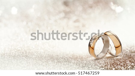 Panoramic banner of two upright gold wedding bands symbolic of love and romance on a textured glitter background with copy space for your greeting or congratulations
