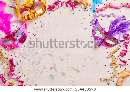 Mardi Gras or carnival frame with brightly colored metallic foil masks with feather decoration and twirled streamers on a pale pink background with copy space