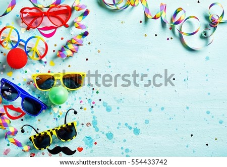 Colorful fun carnival or photo booth accessories with assorted shaped glasses and noses, bright red lips, confetti and streamers forming a side border on light blue textured wood with copy space