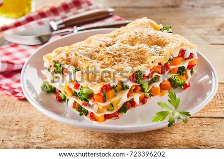 Large portion of healthy colorful vegetable lasagne made with assorted fresh veggies layered with melted mozzarella and pasta served on a white plate
