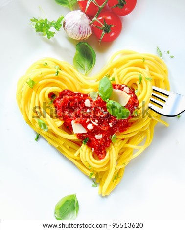 Cooked spaghetti carefully arranged in a heart shape and topped with tomato sauce accompanied by raw ingredients to the side