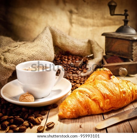Coffee cup with a croissant and fresh coffee beans on a brown background