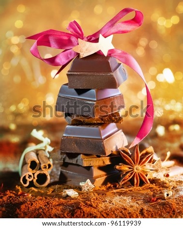 Festive chocolate tower topped with a pink bow and decorated with dried spices and cinnamon against a bokeh of festive lights.