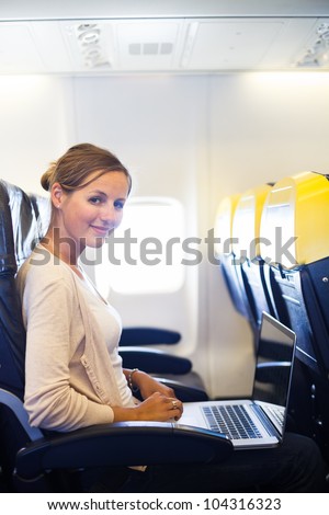 Young woman working on her laptop computer on board of an airplane during the flight