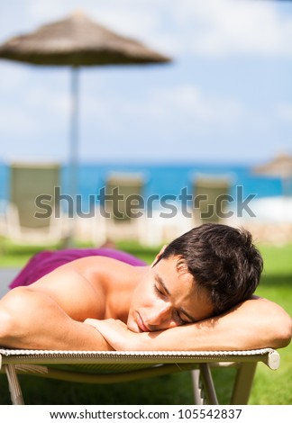 On vacation: young man sunbathing and relaxing on a deckchair near the beach