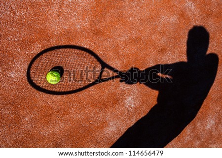 shadow of a tennis player in action on a tennis court (conceptual image with a tennis ball lying on the court and the shadow of the player positioned in a way he seems to be playing it)