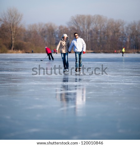 Couple ice skating outdoors on a pond on a lovely sunny winter day