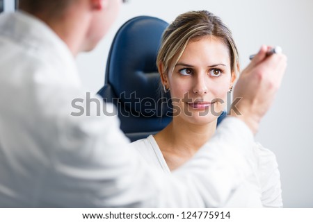 Optometry concept - pretty young woman having her eyes examined by an eye doctor/optometrist (color toned image; shallow DOF)
