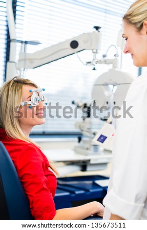 Optometry concept - pretty young woman having her eyes examined by an eye doctor (color toned image; shallow DOF)