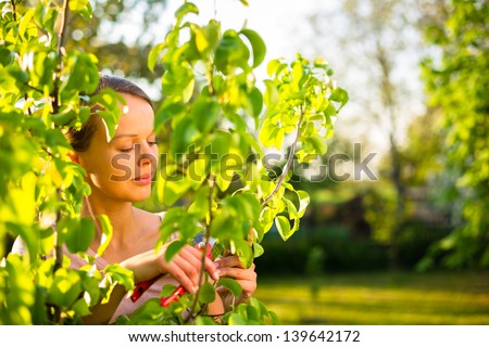Pretty female gardener taking care of her lovely garden on a lovely spring day - cutting branches, double digging/loosening the soil with a spade